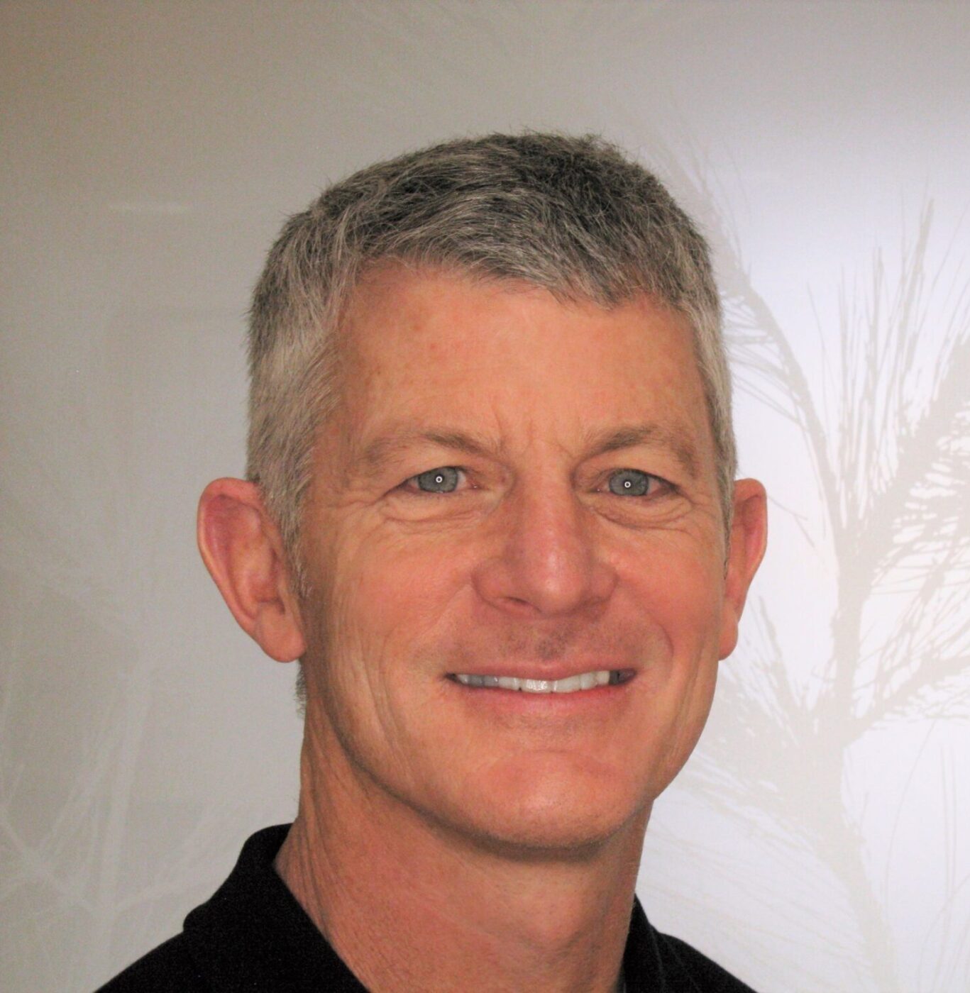 Professional headshot of smiling man in black shirt against neutral background for dental practice website.