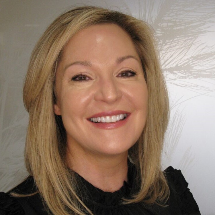 Professional headshot of smiling woman with blonde hair in dental office setting.