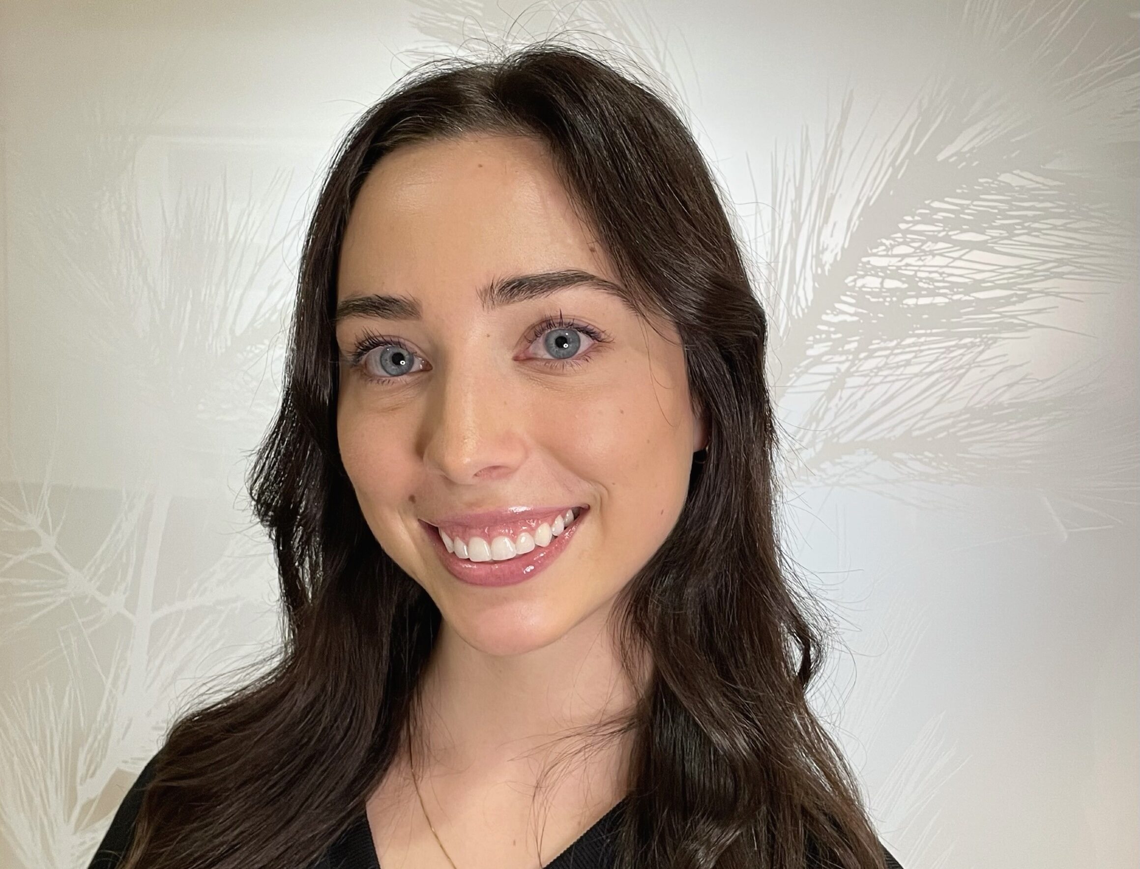 Woman smiling at camera in dental office setting with white background.