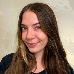 Young woman smiling at camera against white wall background, indoor portrait setting.