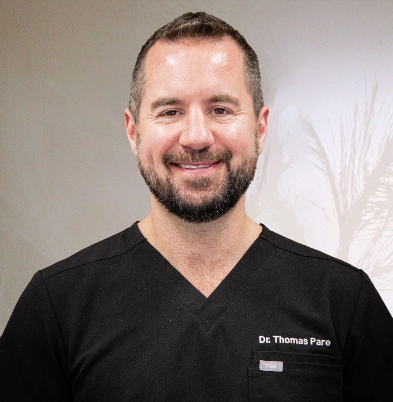 Dr. Thomas Pate smiles in black scrubs against white dental office background.